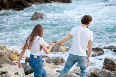 A man and woman are seen walking hand in hand on rocks near the ocean, enjoying a leisurely stroll together.の写真素材