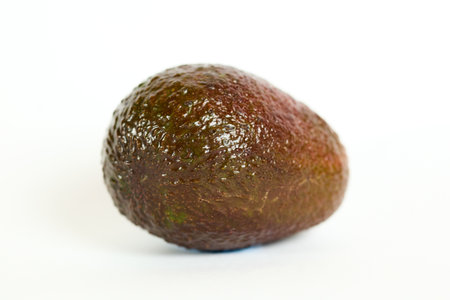 A solitary ripe avocado rests against a stark white backdrop, highlighted by soft lighting that...