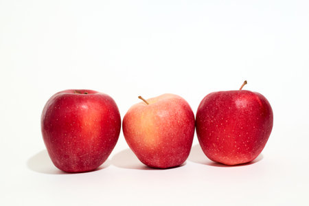 Three ripe, bright red apples are placed side by side on a clean white surface. The apples are...