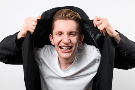 A man is joyfully smiling while holding his jacket over his head, partially shielding himself from the sun or rain.の写真素材