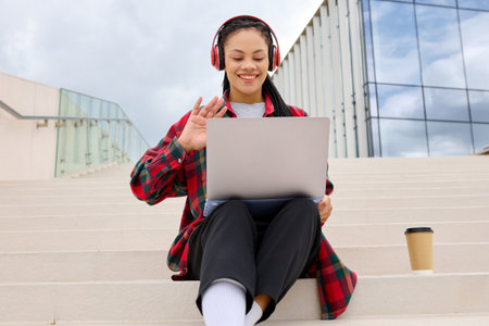 Portrait of a young woman during a video conference with colleagues. Remote work. The manager is sitting on the steps of the building where it was convenient to work.の写真素材