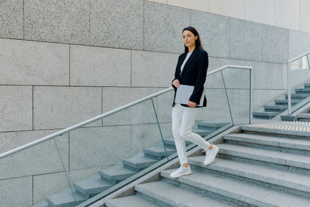 Job interview concept, young woman walking around the city leisurely holding laptop in hands.の写真素材