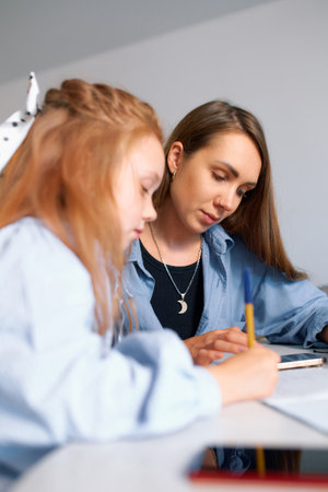 Young mother helps her daughter and checks homework at home at the table.の写真素材