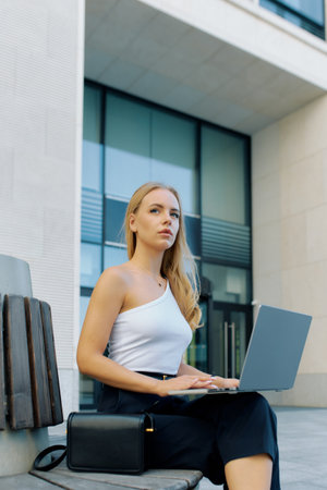 Young slim blonde woman generates ideas for a business project while sitting with a laptop on a bench.の写真素材