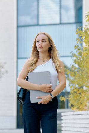 Young slim blonde woman rushing to a business meeting with a laptop in her hands.の写真素材