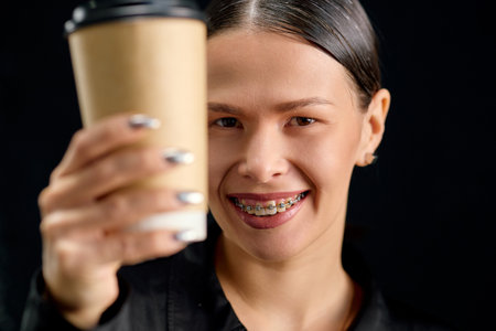 Young woman with braces on her teeth drinks coffee.の写真素材
