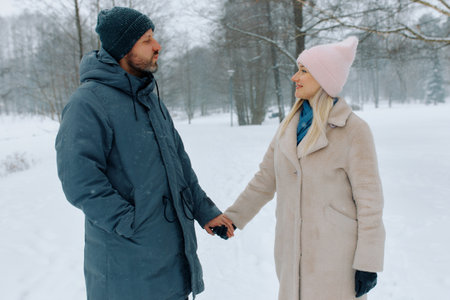 Couple enjoys a winter walk in a snowy park while holding hands on a chilly day.