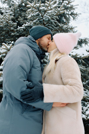 Couple shares a warm kiss in a snowy landscape surrounded by evergreen trees during winter