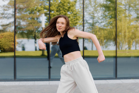 A young woman enjoys dancing outdoors in front of a modern buildingの写真素材