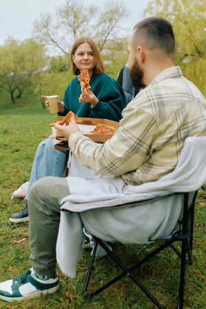 Two friends relax on a grassy area in a park, sharing pizza and drinks. They smile at each other.の写真素材