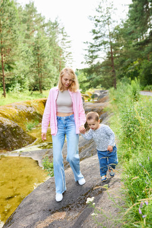 Babysitter and child walk holding hands through the forest.の写真素材