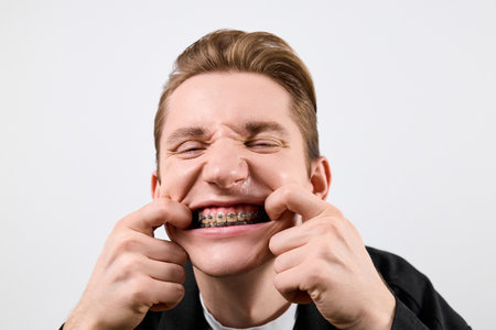 A cheerful young man is pulling his cheeks apart to proudly display his dental braces.の写真素材