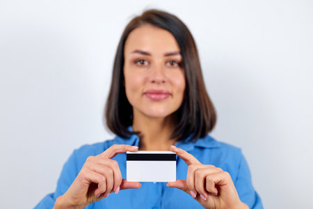 European brunette woman dressed in blue blouse holding laptop and plastic card with mockup.の写真素材