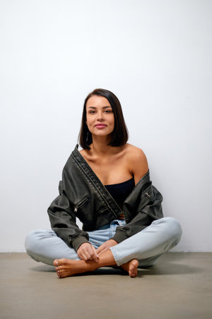 Brunette in a jacket and jeans posing while sitting on the floor.の写真素材
