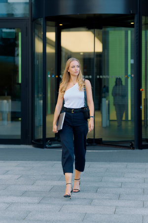 Young slim blonde woman leaves office and goes home with laptop in hands.の写真素材