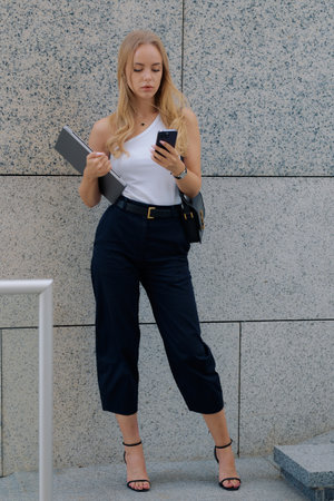 Young pretty woman waiting for meeting and standing on street with laptop.