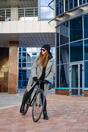 Vertical photo of young urban woman dressed in coat and gloves with bicycle.の写真素材