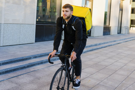 A bearded courier on a bicycle delivers pizza. Delivery around the city during a pandemicの写真素材
