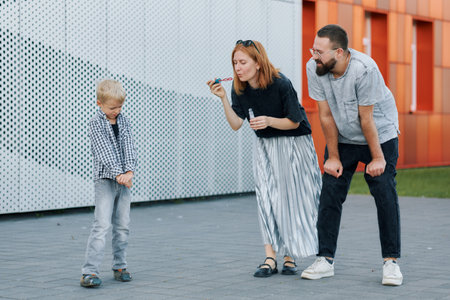 Young family fooling around outside, mom blowing soap bubbles.