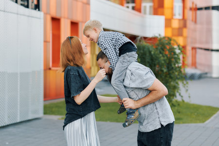 A father lifts his son on his shoulders as the mother shares a joyful moment with them.の写真素材