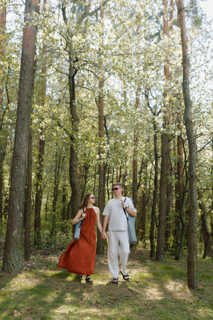 A couple walks hand in hand through a serene forest filled with tall trees and green foliage. Sunlight filters through the leaves.の写真素材
