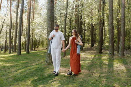 A young couple walks hand in hand through a lush green forest filled with flowering trees, dressed casually in light clothing.の写真素材
