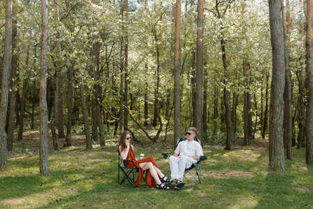 In a tranquil forest during a sunny day, a couple enjoys their time sitting in folding chairs.の写真素材