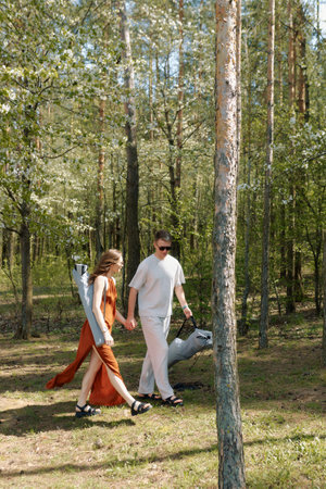 A couple strolls hand in hand through a lush green forest. They are dressed casually and appear relaxed as they walk together.の写真素材