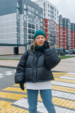 Portrait of a young woman talking on the phone against the background of a residential area.の写真素材