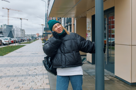 A young stylish woman is talking on the phone standing at the entrance of an apartment building.の写真素材