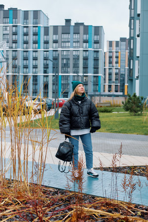 Woman in black jacket walking through modern urban landscape during daylight hours.の写真素材