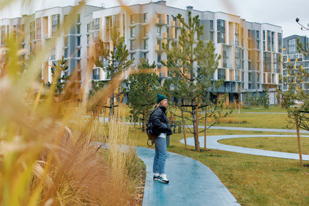 Young woman walking along a path in a park near modern apartment buildings during a cloudy day.の写真素材