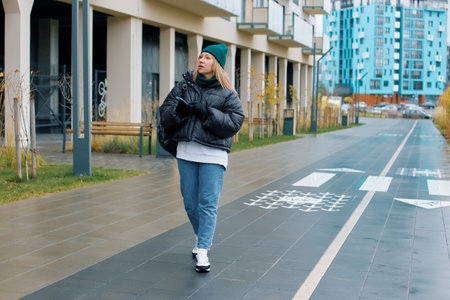 Woman stroll along modern urban pathway wearing casual attire in a vibrant neighborhood.の写真素材