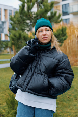 Portrait of a young woman in a jacket and hat who is talking on the phone against the background of...