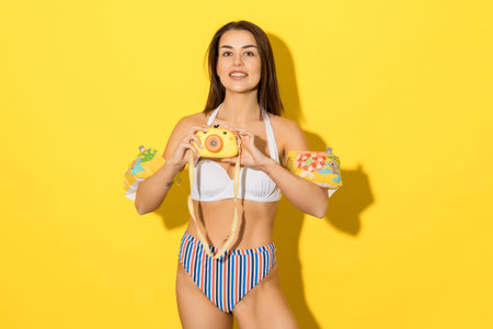 A young woman in a swimsuit with inflatable swimming sleeves on a yellow background.