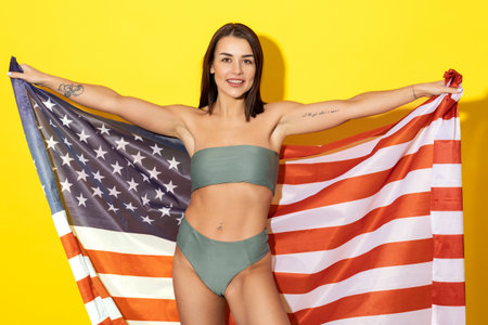 Showcases a beautiful woman, glowing with sun-kissed skin and dressed in a stylish swimsuit adorned with the stars and stripes of the American flagの写真素材