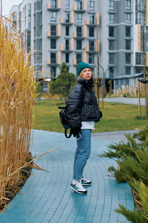 Woman dressed warmly strolling along a path in a contemporary urban park setting.