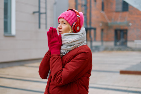 Young woman enjoying music outdoors during chilly weather in a vibrant city neighborhood in...