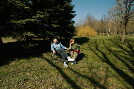A couple relaxes in comfortable folding chairs on a sunny day in a serene outdoor setting.の写真素材