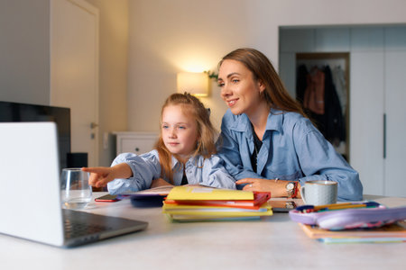 Schoolgirl sits with her mother at home studying a lesson to do homework.