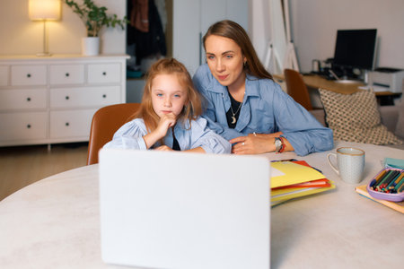 Young schoolgirl with her mother reading electronic resource for homework.の写真素材