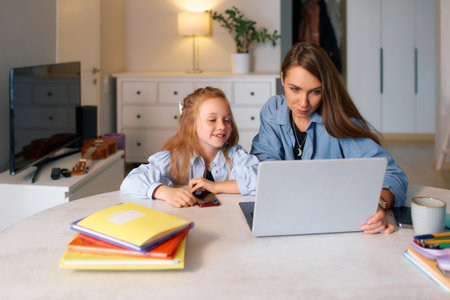 Young mother with her schoolgirl studying remotely while sitting at home.の写真素材