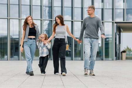 A family consisting of a mother, father and two daughters are walking near a business center.