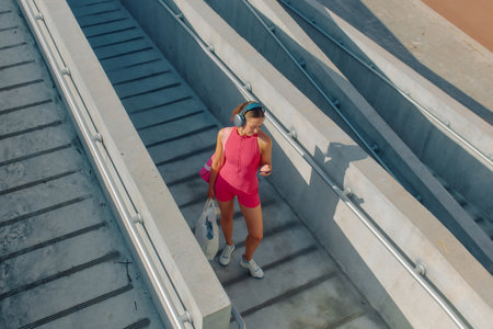 Athletic woman walks down outdoor stairs while checking her phone and wearing headphones.の写真素材