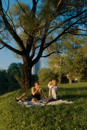 A man and a young woman sit by a pond, enjoying snacks and each other's company.の写真素材
