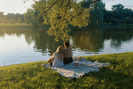 A man and woman share a peaceful picnic by a calm pond surrounded by nature.の写真素材