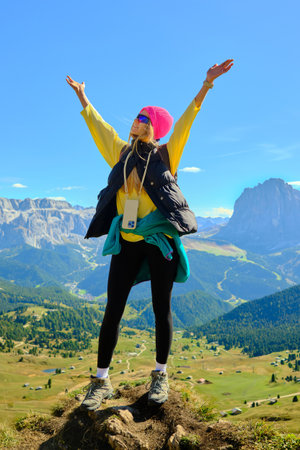 A woman stands atop a mountain, arms raised high, enjoying the sunny weather and beautiful scenery.の写真素材