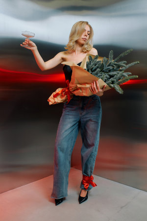 Woman in a chic outfit holds a drink in one hand and a bouquet of fir branches in the other.の写真素材