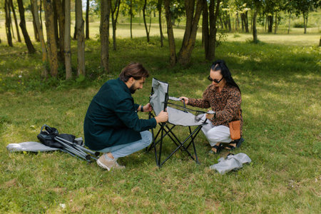 A couple enjoys a beautiful day in the park, working together to set up a picnic chair.の写真素材