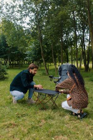 Two friends prepare a picnic in a lush park, surrounded by trees and grass. The atmosphere is cheerful.の写真素材